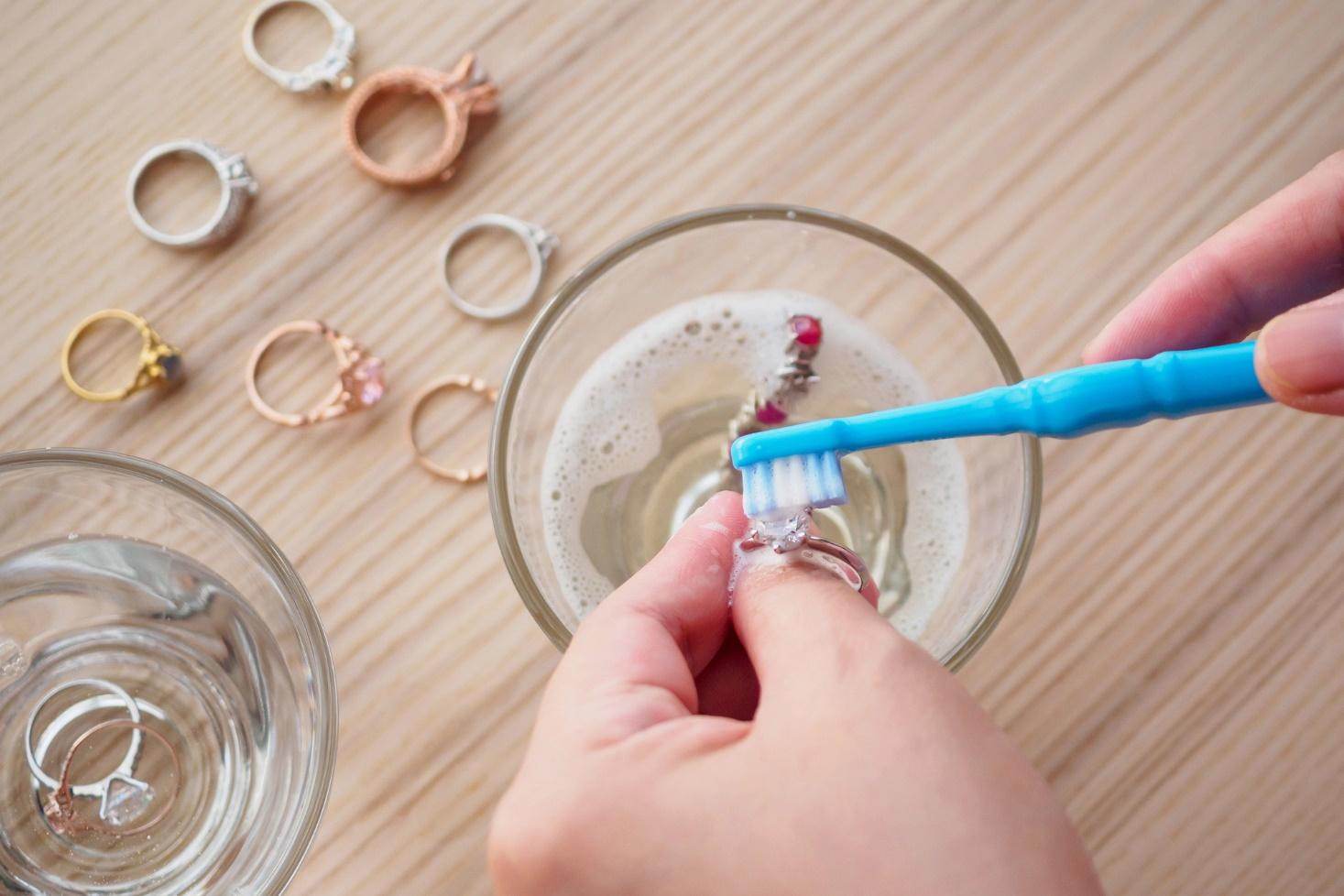 Une personne nettoie des bijoux à l'aide d'une brosse à dents dans de l'eau savonneuse.